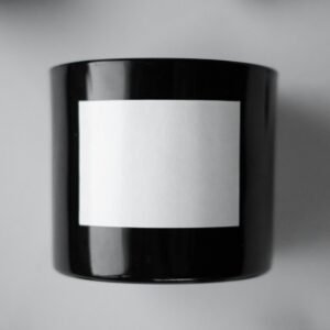 A black candle with blank label surrounded by charcoal, styled in a minimalist setting.